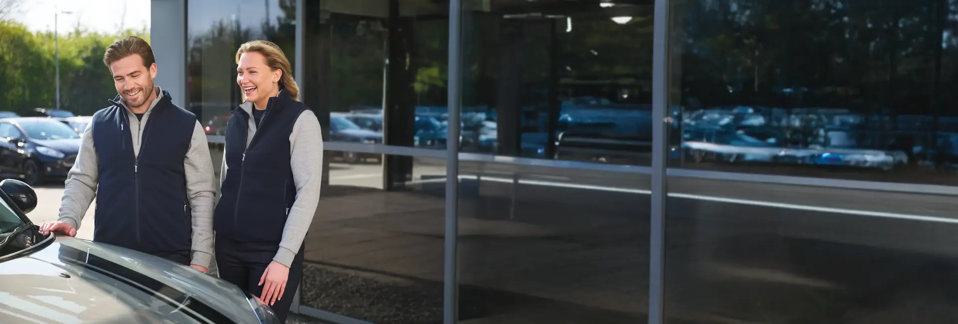 Dame en heer in automotive branch met bedrijfskleding; chino, pullover en bodywarmer